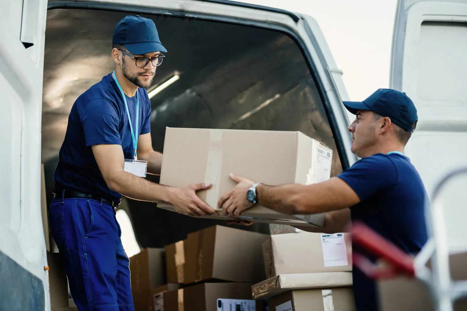 Deux livreurs se passent un carton à l’arrière d’une camionnette